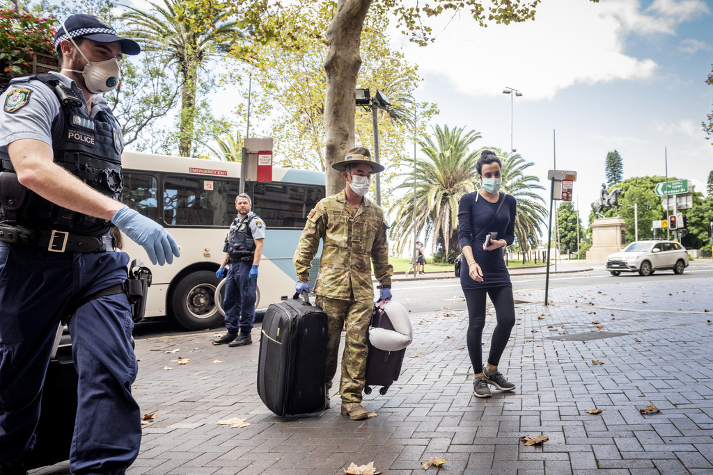 Item 52: Australian overseas travellers, assisted by police and army, arrive via bus direct from the airport for a two-week COVID-19 quarantine at a city hotel, Sydney, New South Wales, 29 March 2020